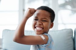 African American boy raising his arm to show how strong he is after getting a vaccination. 