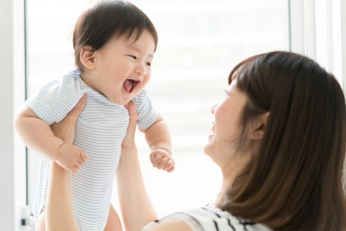 Woman holding up her baby boy as he smiles and laughs.