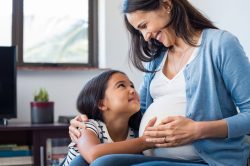 Pregnant mother holds daughter close and daughter feels the tummy of the mother.