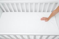 A woman's hand patting a mattress in a crib to check it for firmness. 