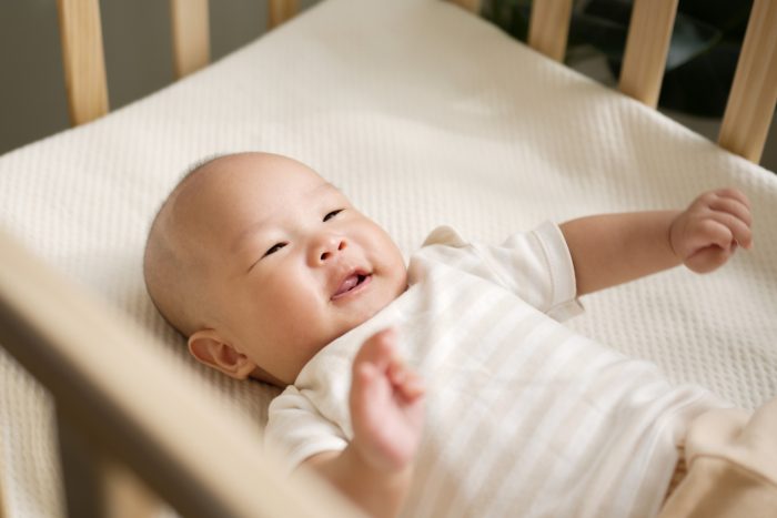 Baby boy lying on his back in a crib smiling at his parent. 