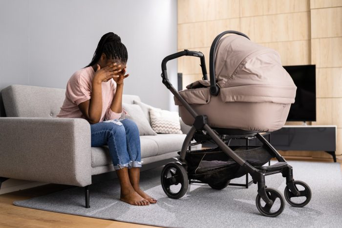 Mom experiencing postpartum depression sits on couch with a baby stroller next to her.