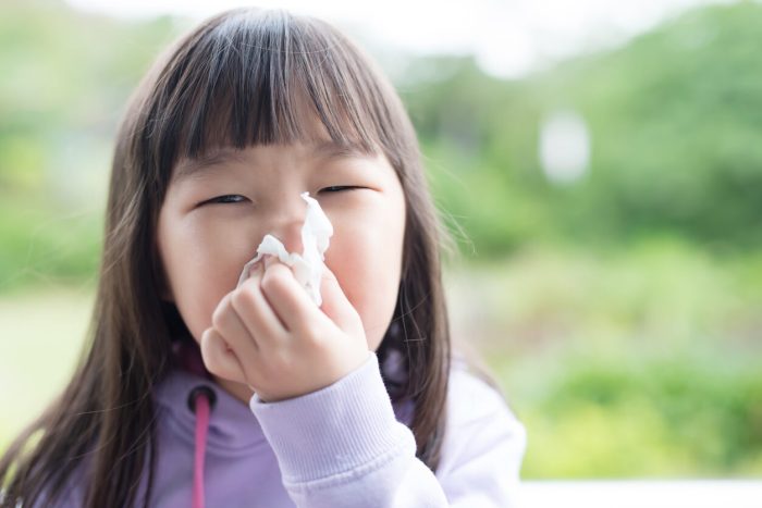 Young child blows her nose, handling one of the most common symptoms of childhood illnesses.