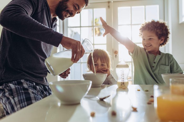 A dad pours milk for his children in the kitchen. 