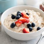 A bowl of oatmeal with blueberries and strawberries is depicted, a great soft food for a child's diet.