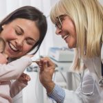 pediatrician touching baby's hand with parent looking on.